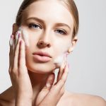 Woman clears a face skin foam on a gray background