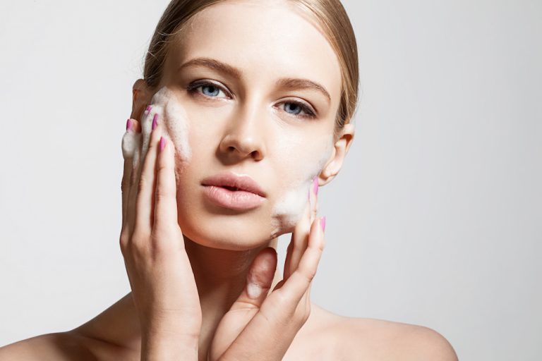 Woman clears a face skin foam on a gray background